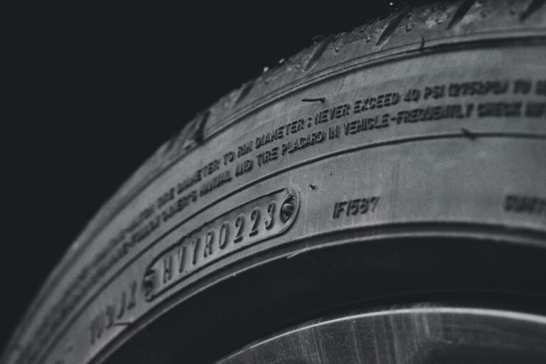 Close-up view of a car tyre showing detailed tread, sidewall markings, and embossed text including a serial number. The surface appears clean with some visible moisture or water droplets.