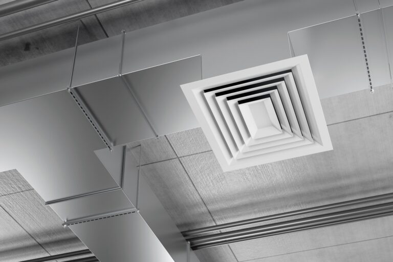 A close-up view of a modern HVAC vent and ductwork on an indoor ceiling, showing metallic pipes, rectangular ducts, and a square air diffuser.